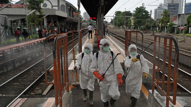 Members of the Indonesian Red Cross Society spray disinfectants on railings on a platform at the Kemayoran train station in Jakarta.