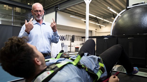 Professor Gordon Waddington explains how the Earth Moon Mars bed works to reporter Elliot Williams. The machine tries to replicate the feeling of different levels of gravity on a person's legs.