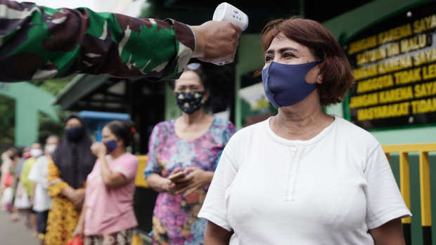 A soldier takes the temperature of a person following social distancing protocols while waiting in line at a rice distribution center at the Central Jakarta Military District Command.