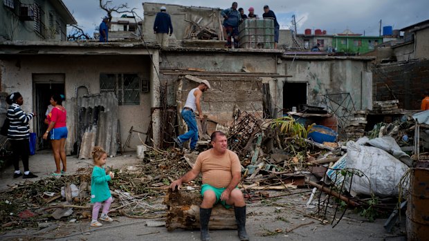 A man rests on the trunk of a tree as he rests from removing rubble from his home in Regla, Cuba.