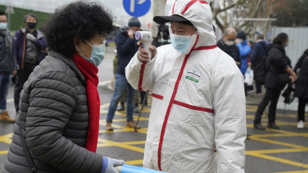 A worker in protective overalls takes the temperature of a woman entering the Hubei Centre for Disease Control and Prevention as the World Health Organisation team makes a visit.