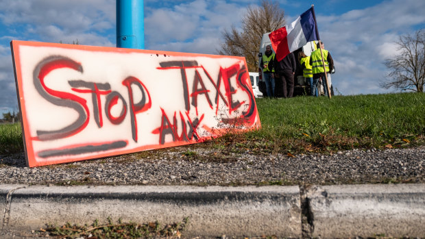 A sign reading "Stop the taxes" sits by the highway behind demonstrators wearing yellow vests (Gilets jaunes) and holding a French national flag during a protest against fuel costs near Rodez, France, on Saturday.
