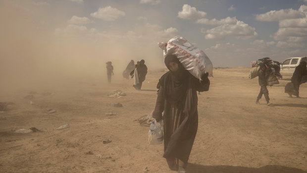 A woman carries supplies from a reception area for people evacuated from the last shred of territory held by Islamic State militants, outside Baghouz, Syria.