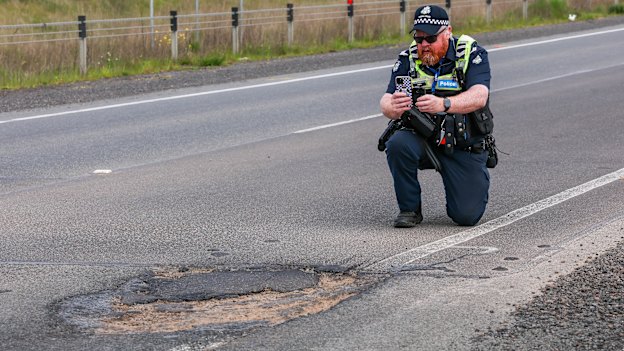 A police officer inspects a pothole near the scene of the crash. 