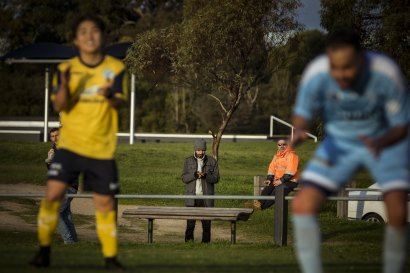 Players celebrate a goal as a data scout working with Genius Sports enters the data into his phone in the Victorian Mens’ State League 1 North-West match between FC Clifton Hill and Corio SC at Quarries Park, Clifton Hill. 