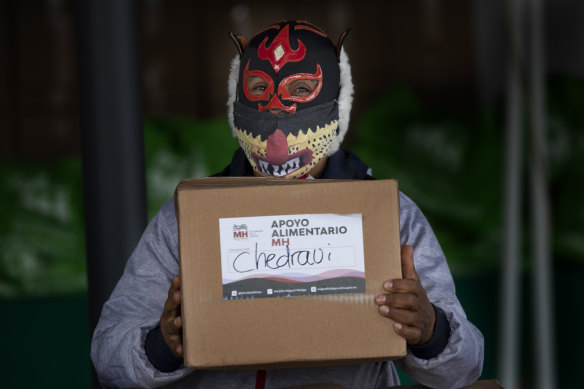Pequeno Felino, a Lucha Libre wrestler, stands ready to hand out a food parcel.