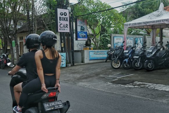 Foreign tourists on a scooter pass by a motorcycle and car rental shop in Kerobokan, Bali. 