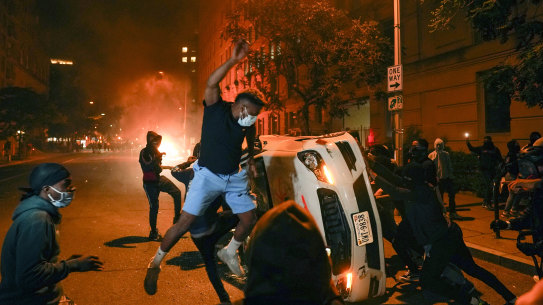 Demonstrators vandalise a car as they protest the death of George Floyd near the White House on Sunday night. 