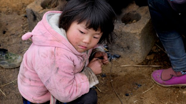 Xia Zhongmei sits at an outdoor furnace in Shanqiao, a village in China's Yunnan province.