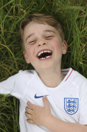 Prince George laughs and frolics on a bed of grass. 
