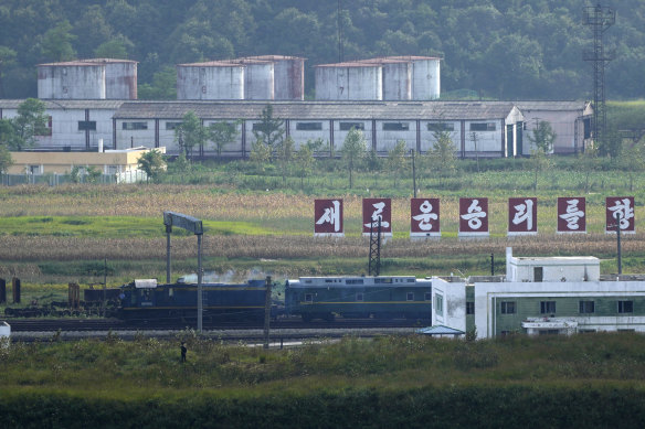 A green train with yellow trimmings, resembling one used by Kim Jong-un, travels past a slogan that reads “towards a new victory” on the North Korea border with Russia and China.