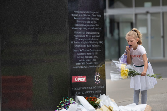 A young fan leaves flowers at the Shane Warne statue.