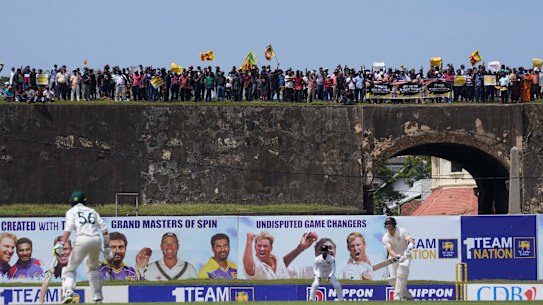 Steve Smith bats while protesters converge atop the Dutch fort behind Galle stadium.