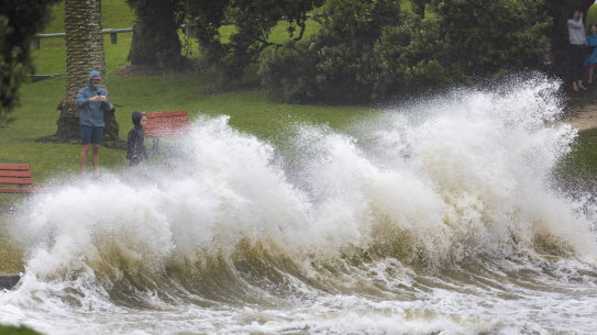 People watch as waves crash against a sea wall at an Auckland beach as a cyclone hits the upper parts of New Zealand.