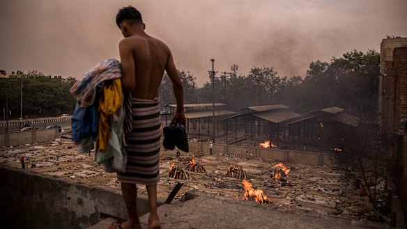 A man does his household chores against the backdrop of burning funeral pyres of the patients who died of the COVID-19 at a crematorium in Delhi.