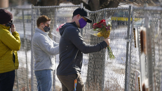 Kiefer Johnson places a bouquet of flowers into a makeshift fence put up around the parking lot outside a King Soopers grocery store where a mass shooting took place a day earlier, in Boulder, Colorado.
