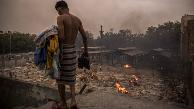 A man does his household chores against the backdrop of burning funeral pyres of the patients who died of the COVID-19 at a crematorium in Delhi.