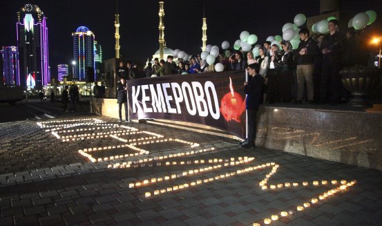 People in the Chechen capital Grozny stand behind banners commemorating the lives lost in the Kemerovo mall fire.