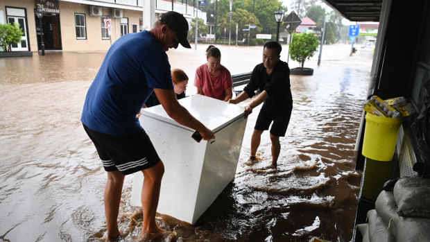 Locals help a Chinese restaurant owner as he tries to salvage a freezer as floodwater inundates his business in Laidley.