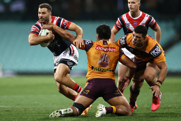Roosters superstar James Tedesco flies past Broncos defenders Joe Ofahengaue and David Fifita.