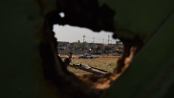 A man pushes a cart along a street past a destroyed car used in a suicide bombing and buildings damaged during the liberation of suburbs in East Mosul from ISIS.