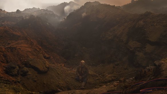 An oilfield worker in Qayyarah takes a break, sitting at the edge of a hole where an oil well fire was recently extinguished.