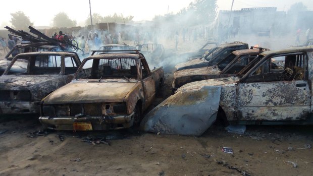 People stand behind burnt out cars following an attack by Boko Haram at a car park in Maiduguri, Nigeria.