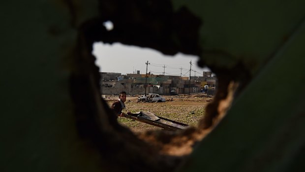 A man pushes a cart along a street past a destroyed car used in a suicide bombing and buildings damaged during the liberation of suburbs in East Mosul from ISIS.