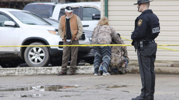 An officer stands guard as people comfort each other near the scene of a fatal shooting at a car wash in Pennsylvania.