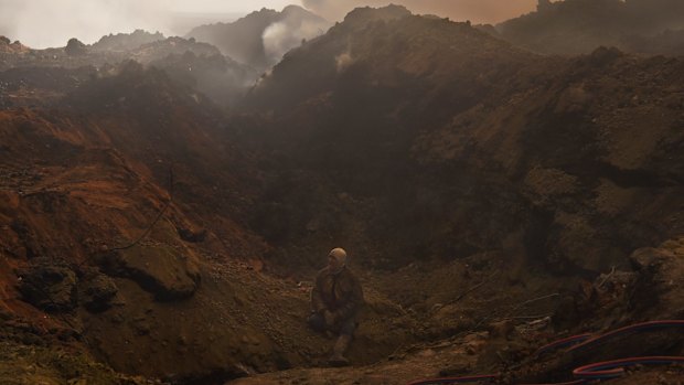 An oilfield worker in Qayyarah takes a break, sitting at the edge of a hole where an oil well fire was recently extinguished.