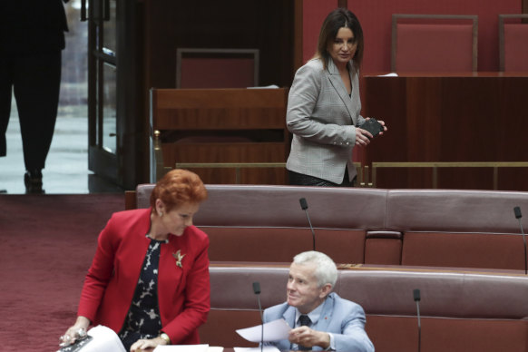 Senator Jacqui Lambie walks past Senators Pauline Hanson and Malcolm Roberts.
