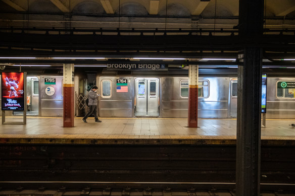 A commuter wearing a protective mask walks past a train on a subway platform in New York.