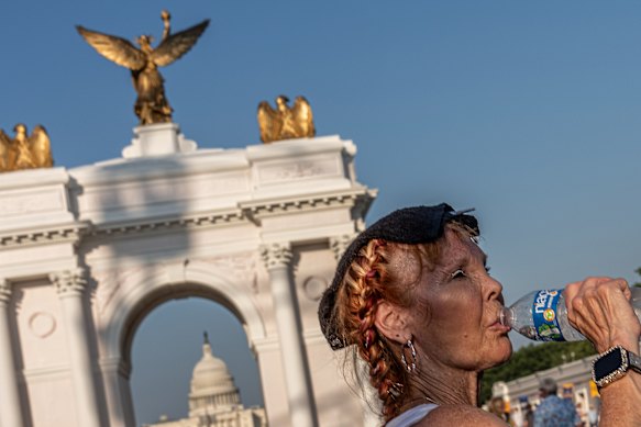 A woman drinks water in front of Donald Trump’s proposed Triumphal Arch at the Great American State Fair during an extreme heat wave on the National Mall in Washington. 