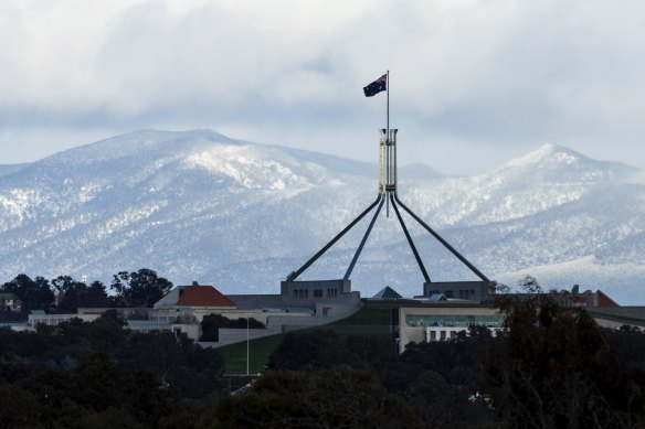 Parliament House in Canberra with snow on the mountains behind on June 1.