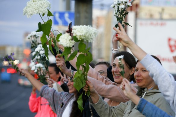 Women wave flowers as they join protest against the Belarus election results on August 13.