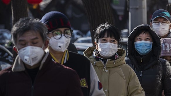 Chinese customers wear protective masks as they line up single file to buy dumplings at a popular local shop in Beijing, China.