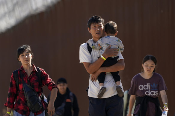 A group of people, including many from China, walk along the wall after crossing from Mexico into the US to seek asylum last month.