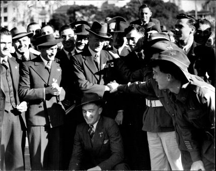 “A year after General Bennett’s ordeal before Royal Commission, soldiers and returned men gather affectionately round him in the Sydney Domain.”