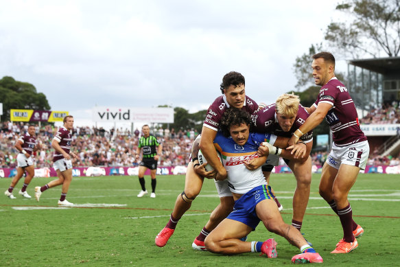 Manly defenders drag Canberra winger Xavier Savage towards the sideline.