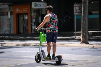 A Lime e-scooter rider in the CBD travels without wearing the available helmet.