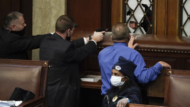 Police with guns drawn watch as protesters try to break into the House chamber.