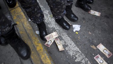One hundred Bolivar bills lay on the ground close to the boots of several police officers, after they were thrown by protesters during a protest against the government of President Nicolas Maduro, in Caracas, Venezuela.