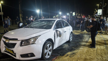 An Israeli police officer inspects the damaged car of an Israeli Arab man who was attacked and injured by an Israeli Jewish mob in Bat Yam, Israel.