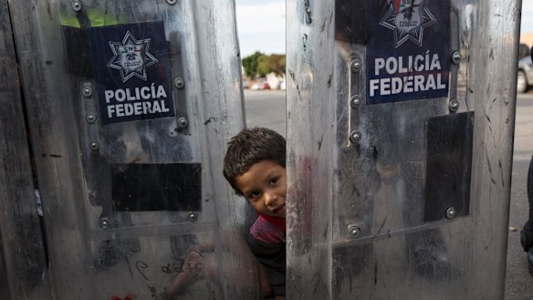 Elias Lopez, a three-year-old Honduran migrant, plays in between the shields of a line of Mexican riot police in Tijuana, Mexico.