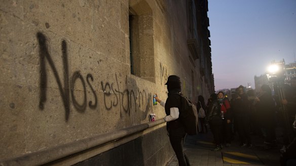 A protester sprays the "They're killing us" on the exterior of the National Palace in Mexico City.