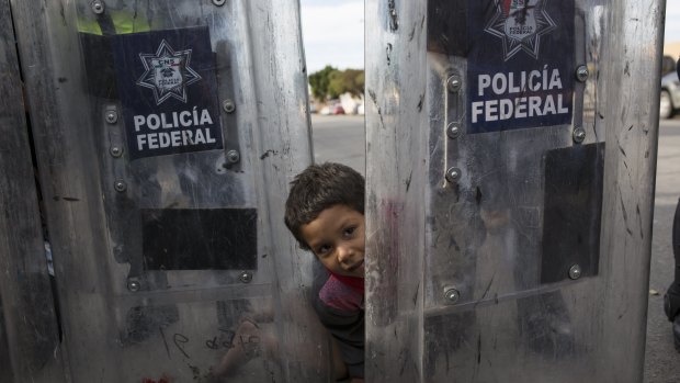 Elias Lopez, a three-year-old Honduran migrant, plays in between the shields of a line of Mexican riot police in Tijuana, Mexico.