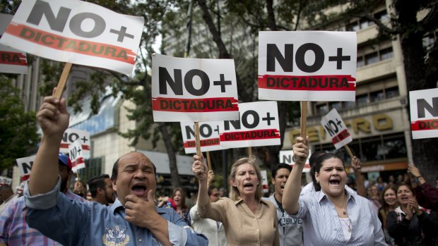 People holding signs with a message that reads in Spanish: "No more dictatorship" take part in a walk out against President Nicolas Maduro, in Caracas, Venezuela.