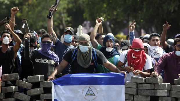 Masked protesters, one with a Nicaraguan flag, yell from the road block they erected as they face off with security forces near the University Politecnica de Nicaragua in Managua on Saturday.