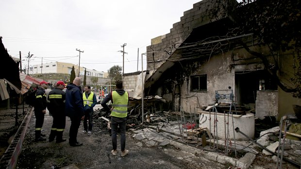 A volunteer stands with firemen in the burnt school for refugee children, part of the One Happy Family project on the island of Lesbos, Greece.