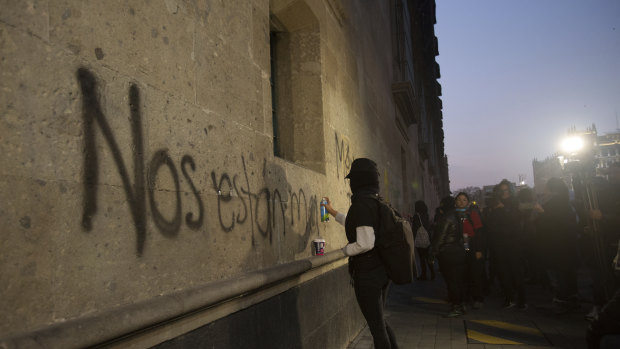 A protester sprays the "They're killing us" on the exterior of the National Palace in Mexico City.